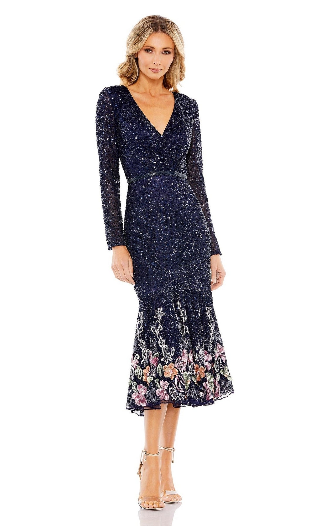 A woman in the Mac Duggal 5589 Beaded Midi Wedding Guest Dress—navy, plus size, long sleeves with sparkling embellishments and floral embroidery at the hem—pairs it with strappy heels for an elegant occasion or wedding.